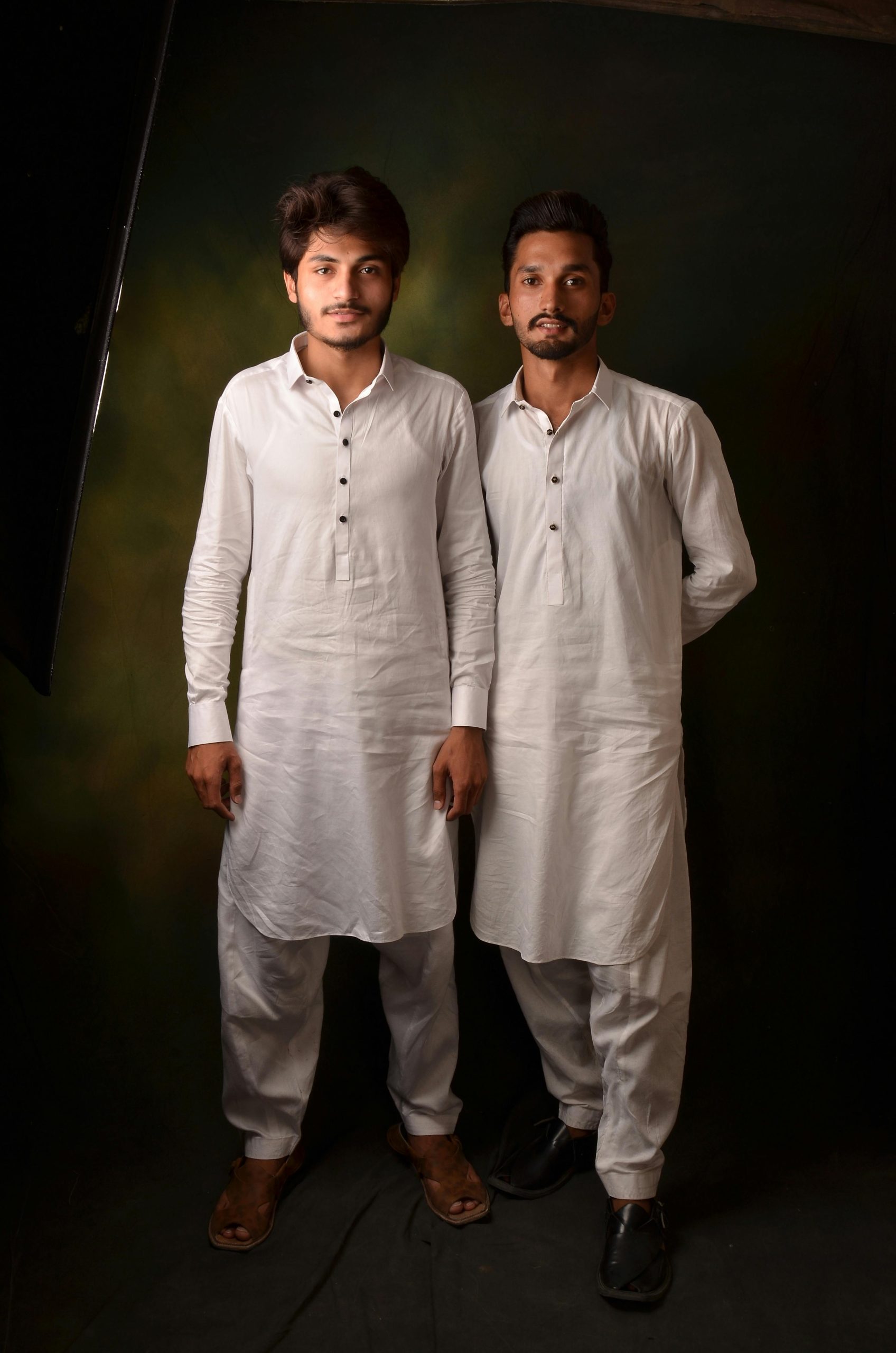 Two men in white traditional clothing posing in a studio.